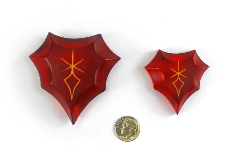 May include: Two red, crystal-like shields with a gold symbol in the center. The shields are different sizes.