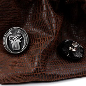 May include: A brown leather dice bag with a skull and crossbones design on a metal charm. The bag has a drawstring closure.