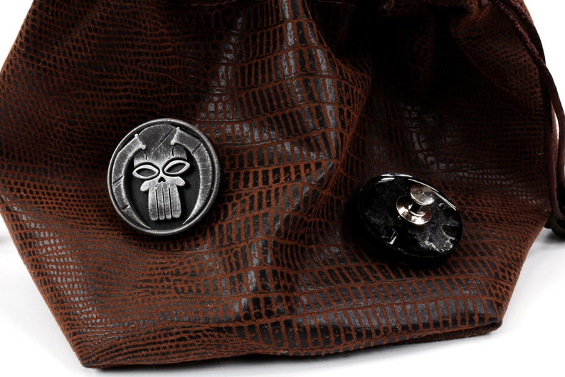 May include: A brown leather dice bag with a skull and crossbones design on a metal charm. The bag has a drawstring closure.