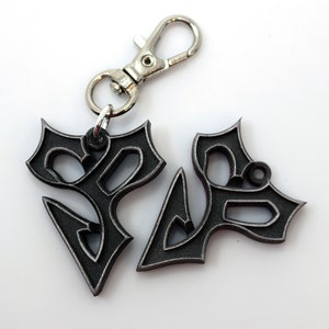 May include: A black metal keychain with a stylized design. The keychain has a silver metal clasp.