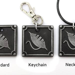 Puede incluir: Tres colgantes de metal plateado con un dise&ntilde;o de hoja estilizado. Los colgantes se muestran en tres estilos diferentes: est&aacute;ndar, llavero y collar.
