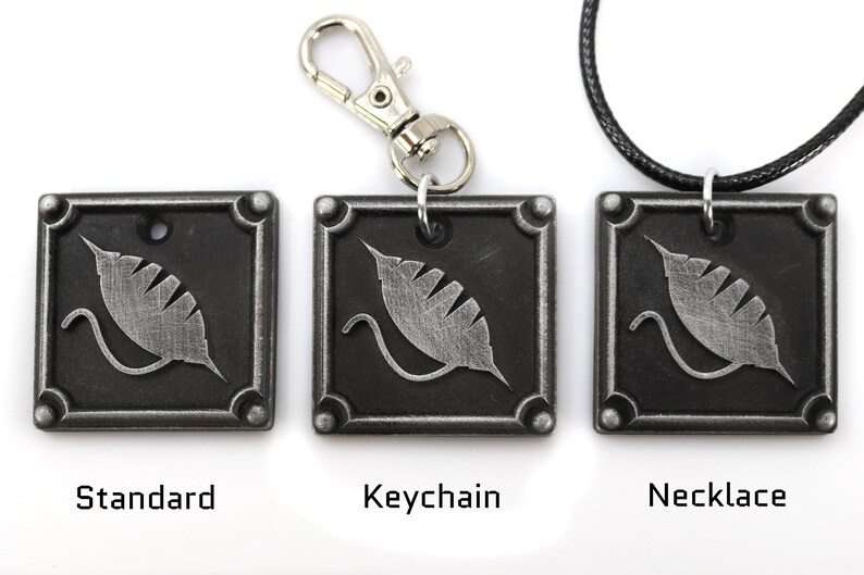Puede incluir: Tres colgantes de metal plateado con un dise&ntilde;o de hoja estilizado. Los colgantes se muestran en tres estilos diferentes: est&aacute;ndar, llavero y collar.
