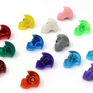 May include: A collection of twelve colorful, translucent, plastic pins with a constellation design. Each pin is shaped like a crescent moon and features a different color, including red, orange, yellow, green, blue, purple, pink, and gray.