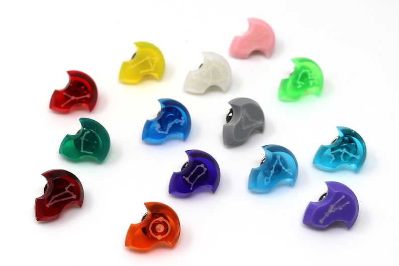 May include: A collection of twelve colorful, translucent, plastic pins with a constellation design. Each pin is shaped like a crescent moon and features a different color, including red, orange, yellow, green, blue, purple, pink, and gray.