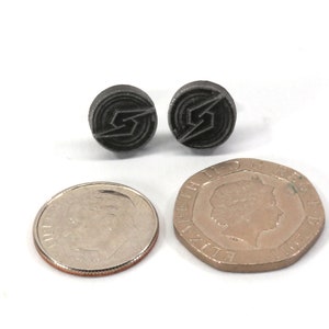 May include: A pair of black metal earrings featuring a stylised lightning bolt design. The earrings are shown next to a US dime and a British one pound coin for size comparison.