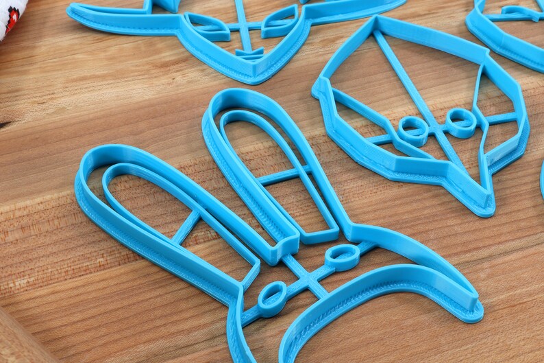 May include: A set of blue plastic cookie cutters in various shapes, including a bunny, a spaceship, and a geometric design. The cutters are on a wooden surface.