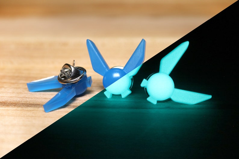 Peut inclure: Deux &eacute;pingles bleu phosphorescentes en forme de Triforce de la s&eacute;rie de jeux vid&eacute;o The Legend of Zelda. Les &eacute;pingles sont pr&eacute;sent&eacute;es &agrave; la fois en lumi&egrave;re normale et dans le noir, mettant en &eacute;vidence leur fonction phosphorescente.