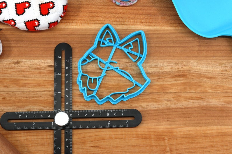 K&ouml;nnte beinhalten: Ein blauer Plastik-Ausstecher in Form eines Hundekopfes. Der Ausstecher liegt auf einer Holzoberfl&auml;che mit einem Lineal.
