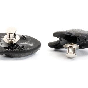 Op de afbeelding: Twee zwarte plastic drukknopen met zilveren metalen stiften. De drukknopen zijn gevormd als een vis met een afgeronde kop en een platte staart.