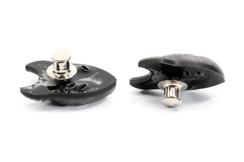 Op de afbeelding: Twee zwarte plastic drukknopen met zilveren metalen stiften. De drukknopen zijn gevormd als een vis met een afgeronde kop en een platte staart.