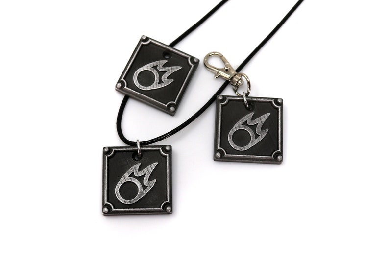 May include: Three silver and black metal pendants with a flame design. The pendants are on a black cord and a silver key chain.