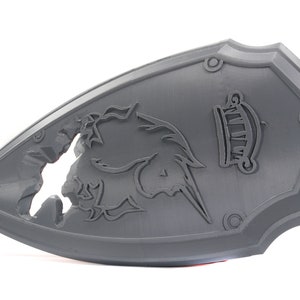 May include: A gray plastic shield with a unicorn design and the word "WIZARD" in a banner. The shield has a broken, cracked design.