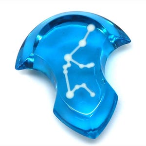 Op de afbeelding: Een blauwe glazen hanger met een witte omtrek van het sterrenbeeld Waterman.