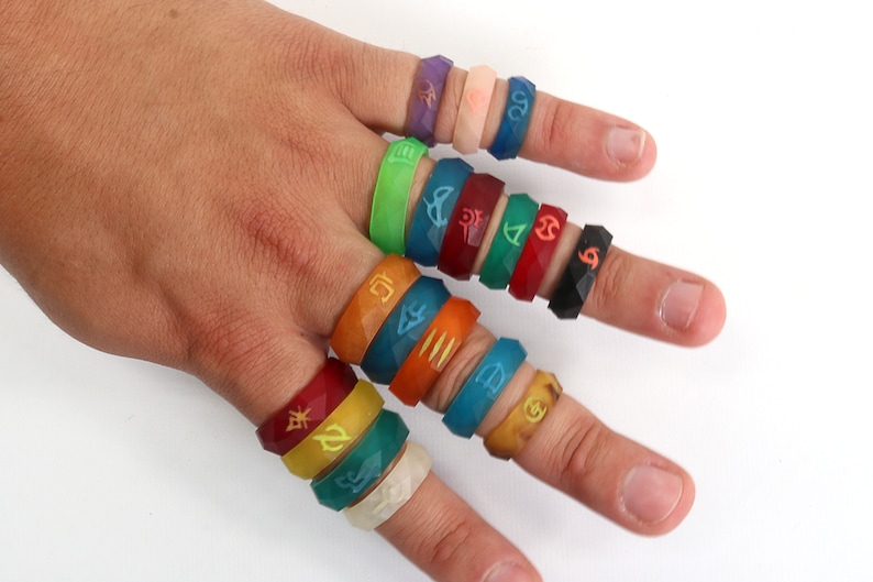 May include: A hand wearing a variety of colorful silicone rings with different symbols and designs. The rings are stacked on each finger.