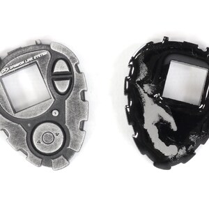May include: A silver and black Digimon toy with a screen and buttons. The toy is in two states, one with a clean surface and the other with a worn surface.