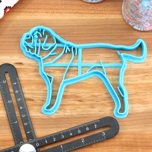 Peut inclure: Un emporte-pi&egrave;ce en plastique bleu en forme de chien. L'emporte-pi&egrave;ce est sur une surface en bois avec une r&egrave;gle et un pot de p&eacute;pites en arri&egrave;re-plan.