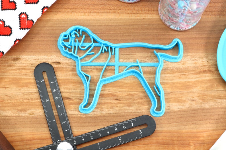 Peut inclure: Un emporte-pi&egrave;ce en plastique bleu en forme de chien. L'emporte-pi&egrave;ce est sur une surface en bois avec une r&egrave;gle et un pot de p&eacute;pites en arri&egrave;re-plan.