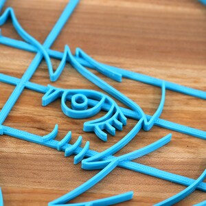 May include: A close-up of a blue 3D printed design of a face with an eye, eyelashes, and a nose. The design is made of multiple layers of plastic.