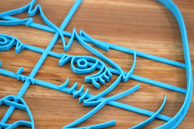 May include: A close-up of a blue 3D printed design of a face with an eye, eyelashes, and a nose. The design is made of multiple layers of plastic.