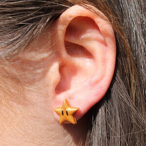 May include: A gold star-shaped earring with a black outline and two black dots in the center.