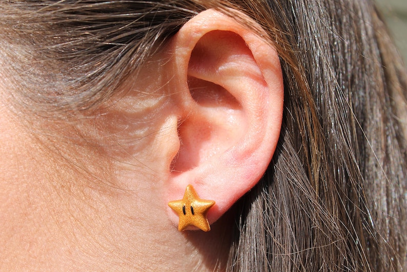 May include: A gold star-shaped earring with a black outline and two black dots in the center.