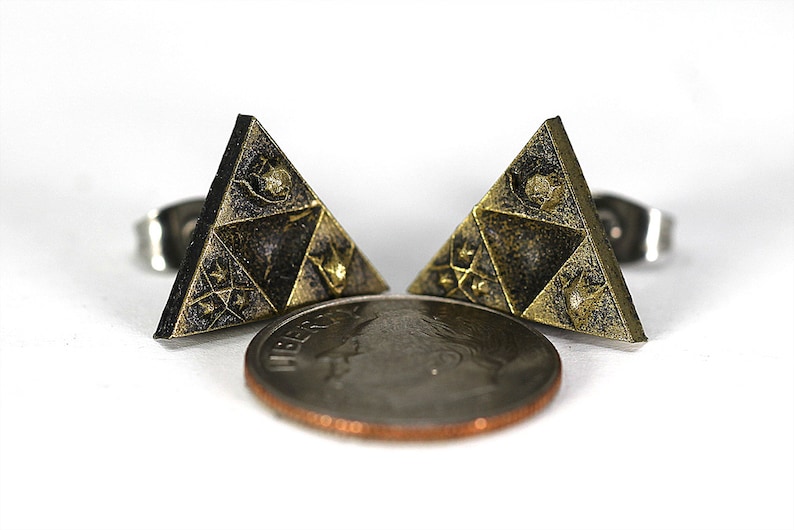 May include: A pair of gold-toned triangle earrings with a black and gold design. The earrings are about the size of a US penny.