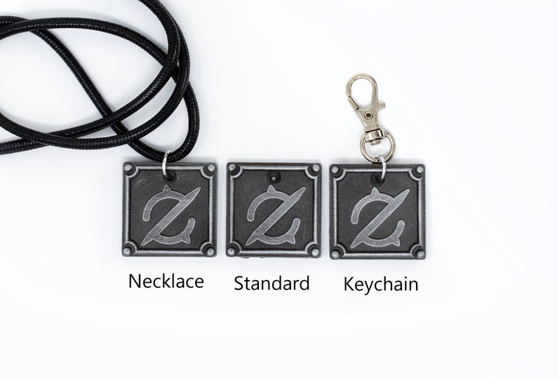 Pu&ograve; includere: Tre ciondoli color argento con un design stilizzato della lettera Z. I ciondoli sono mostrati su una collana con cordoncino nero, un ciondolo standard e un portachiavi.