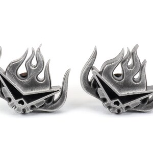 May include: A pair of silver-colored metal earrings featuring a stylized flame design with a skull and crossbones inside. The earrings are a popular anime and manga inspired design.