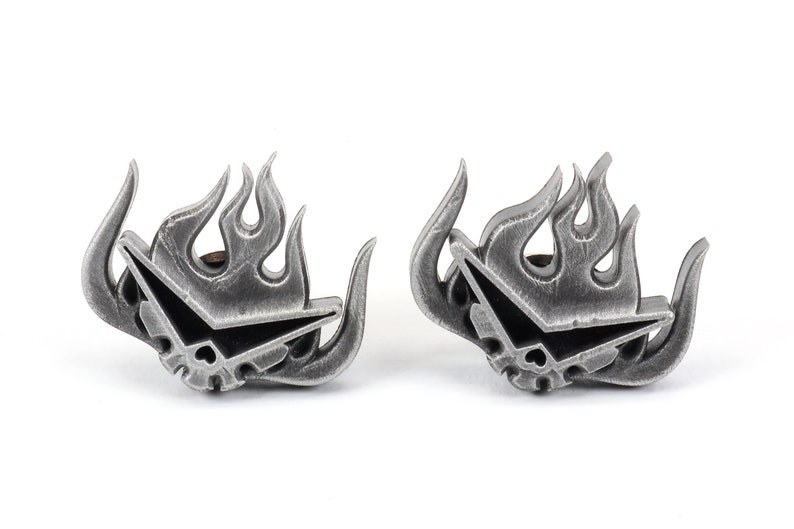 May include: A pair of silver-colored metal earrings featuring a stylized flame design with a skull and crossbones inside. The earrings are a popular anime and manga inspired design.
