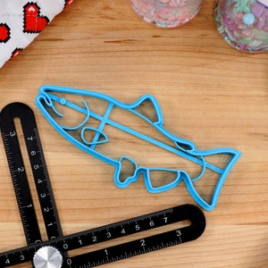 May include: A blue plastic fish-shaped cookie cutter on a wooden surface. The cutter is about 7 inches long.