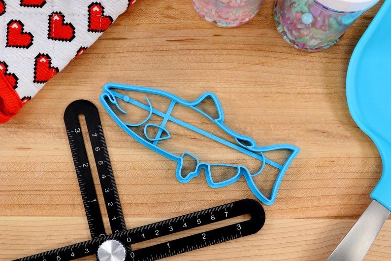 May include: A blue plastic fish-shaped cookie cutter on a wooden surface. The cutter is about 7 inches long.