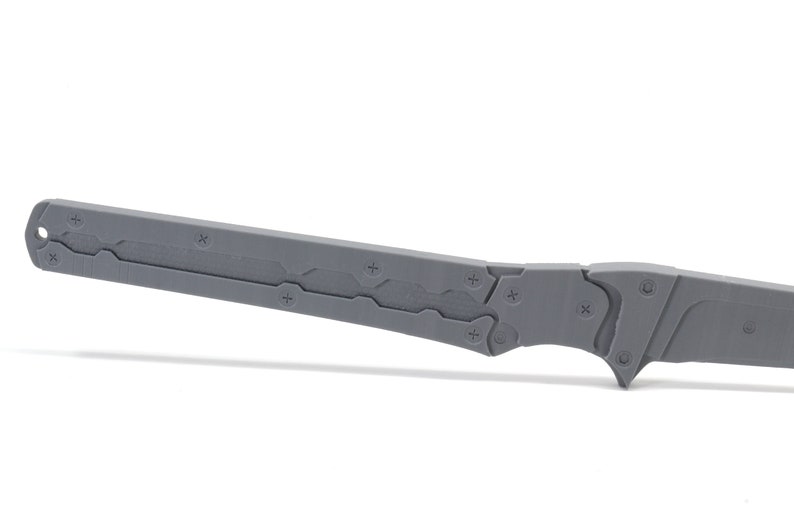 May include: A gray metal knife with a textured blade and a black handle. The knife has a sharp point and a serrated edge.