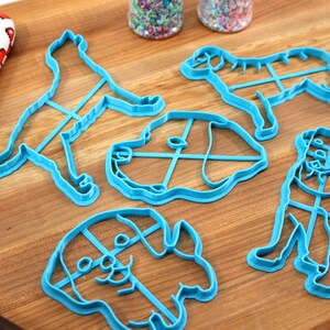 Peut inclure: Cinq emporte-pi&egrave;ces en forme de chien en plastique bleu sur une surface en bois. Les emporte-pi&egrave;ces sont de diff&eacute;rentes tailles et formes, notamment un chien debout, un chien assis et une t&ecirc;te de chien.