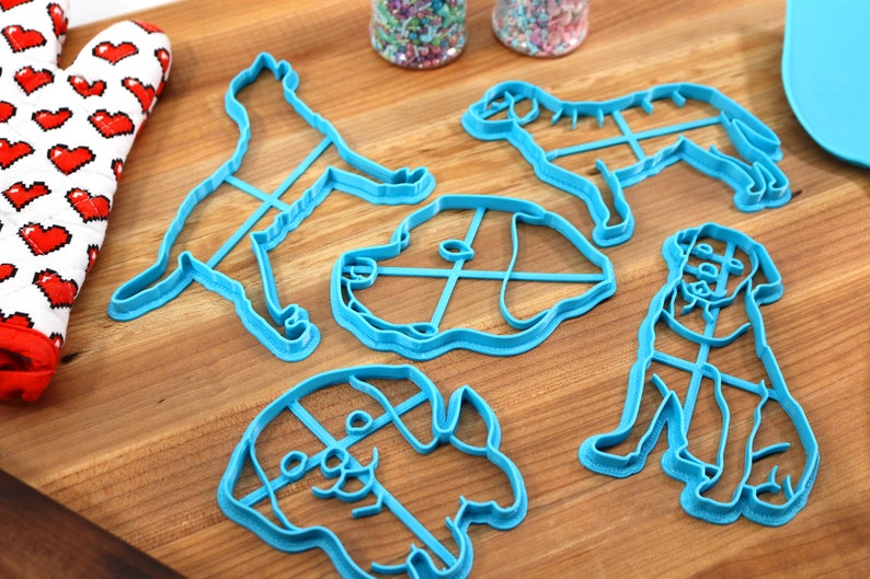 Peut inclure: Cinq emporte-pi&egrave;ces en forme de chien en plastique bleu sur une surface en bois. Les emporte-pi&egrave;ces sont de diff&eacute;rentes tailles et formes, notamment un chien debout, un chien assis et une t&ecirc;te de chien.
