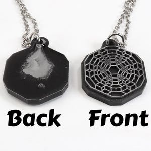 May include: A silver chain necklace with a black octagonal pendant. The front of the pendant features a silver geometric design. The back of the pendant is plain.