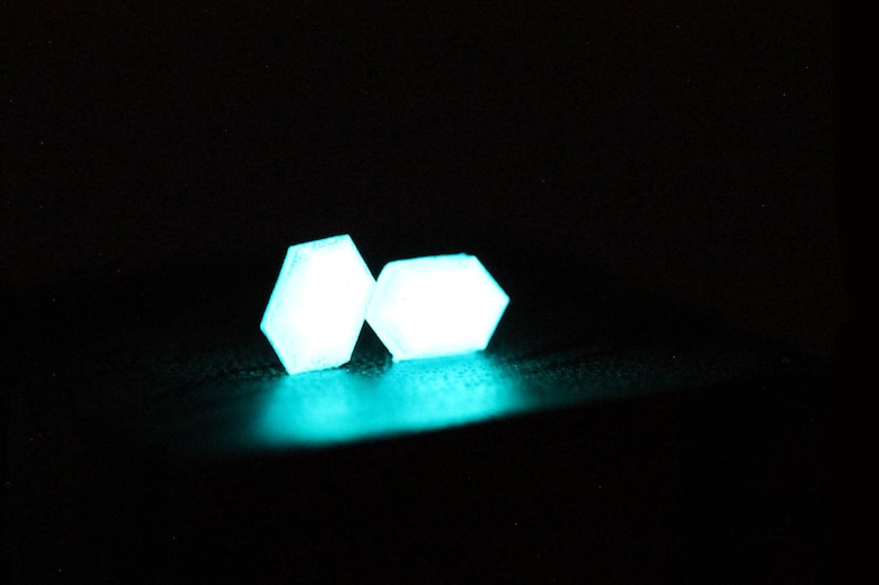 K&ouml;nnte beinhalten: Zwei leuchtende, sechseckige Formen in Teal auf schwarzem Hintergrund.
