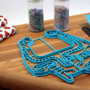 Peut inclure: Un emporte-pi&egrave;ce en plastique bleu en forme de personne avec un design d&eacute;taill&eacute;. L'emporte-pi&egrave;ce est sur une surface en bois avec un rouleau &agrave; p&acirc;tisserie, des vermicelles dans des bocaux et un tapis de d&eacute;coupe bleu.