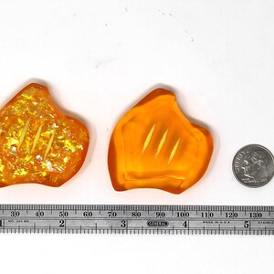 May include: Two orange, leaf-shaped resin pieces with three parallel grooves, next to a dime and a ruler. The resin pieces have a glittery, iridescent effect. The ruler shows measurements in inches.