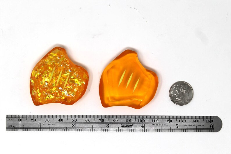 May include: Two orange, leaf-shaped resin pieces with three parallel grooves, next to a dime and a ruler. The resin pieces have a glittery, iridescent effect. The ruler shows measurements in inches.