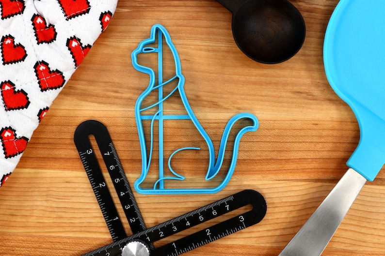 May include: A blue plastic cat-shaped cookie cutter on a wooden surface. The cutter has a detailed design and is perfect for making cat-shaped cookies.