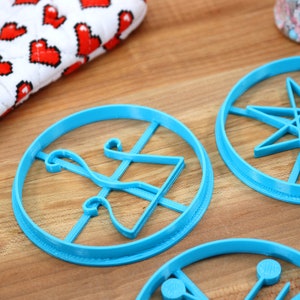 May include: Four blue plastic cookie cutters on a wooden surface. The cutters are shaped like a star, a bell, a geometric design, and a circle with a line through it.