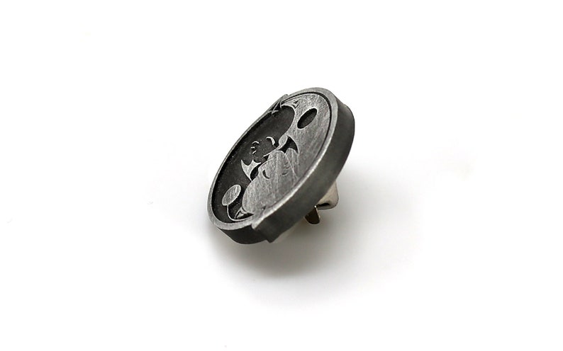 May include: A silver-toned metal pin with a black and white design of a cartoon character. The character is a creature with large eyes and a wide mouth.