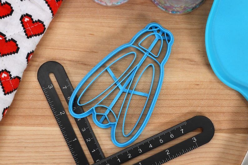 May include: A blue plastic cookie cutter shaped like a dragonfly. The cutter has a detailed design with intricate wings and a body.