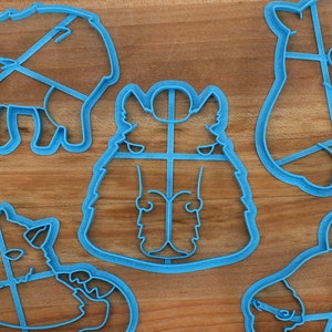 May include: Five blue plastic cookie cutters shaped like different animals. The cutters are on a wooden surface.