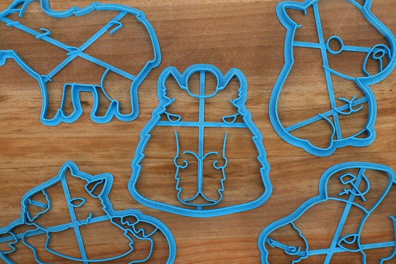 May include: Five blue plastic cookie cutters shaped like different animals. The cutters are on a wooden surface.