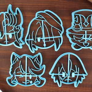 May include: Five blue plastic cookie cutters shaped like cartoon characters. Each cutter has a different facial expression and hairstyle.