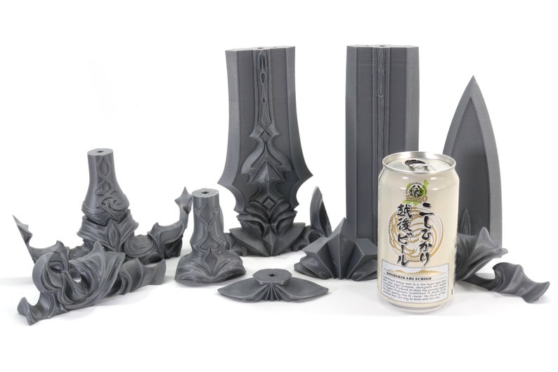 May include: A set of 3D printed gray plastic pieces that make up a sword. The pieces are arranged on a white surface with a can of Japanese beer in the center.
