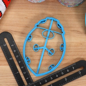 May include: A blue plastic ladybug cookie cutter. The cutter is shaped like a ladybug with a round body and six legs. There are five small circles on the body of the ladybug.