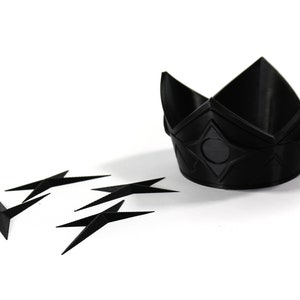 May include: A black plastic crown with a geometric design and a black circle in the center. Five black plastic stars are scattered around the crown.