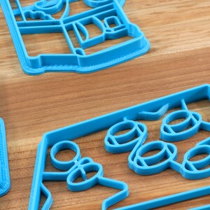 May include: Three blue plastic cookie cutters, one shaped like a house, one shaped like a star, and one shaped like a group of circles.